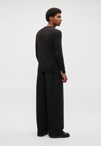 Černý pletený svetr s dlouhým rukávem v kombinaci s širokými černými kalhotami. Svetr má kulatý výstřih a žebrované manžety. Minimalistický design.