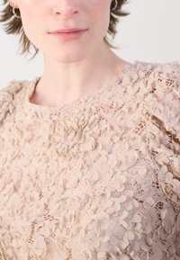 Beige Spitze Oberteil mit floralen Mustern, strukturierten Details und kurzen Puffärmeln, rundem Ausschnitt und aufwendigen Stoffschichten.