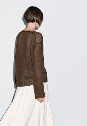 Brun stickad tröja med långa ärmar och ribbad fåll, kombinerad med en flödande vit kjol, sedd bakifrån mot en ljus bakgrund.