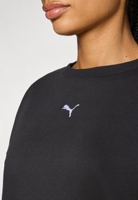 Sudadera negra con cuello redondo y un pequeño logo de Puma en color lila bordado en el pecho. Material suave de mezcla de algodón.