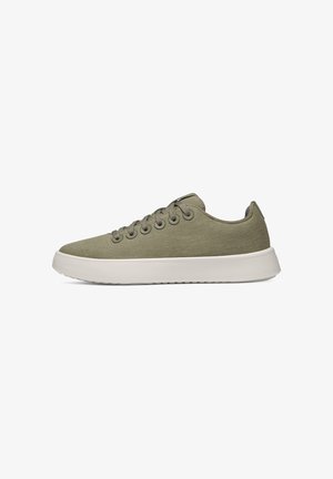 Niedriger Sneaker aus olivgrünem Canvas mit weißer dicker Gummisohle und runden Ösen auf weißem Hintergrund.