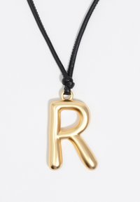 Kuldmetallist tähestik "R" ripats rippub musta nahkpaela küljes, millel on sile ja läikiv pind ning ümar ja mänguline disain.