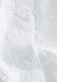 White fabric with raised floral embroidery and two white buttons along a vertical seam.