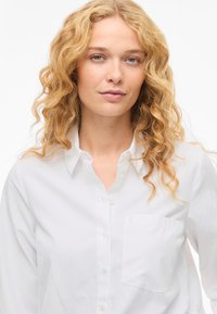 Vit skjorta med knappar i en bomullsblandning, med spetsig krage, långa ärmar och en bröstficka. Mjuk textur med en slät yta.