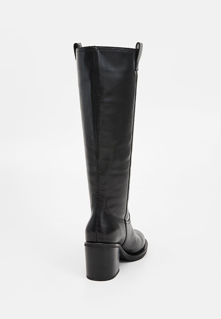 Czarny, skórzany kozak sięgający do kolan z blokowym obcasem, o gładkiej fakturze i przeszyciami. Z tyłu rozcięcie ułatwiające zakładanie.