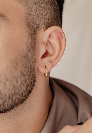 Goldene Creolen an der Ohrmuschel eines kurz geschorenen, bärtigen Ohres, mit glatter Oberfläche und kreisförmiger Form, teilweise von Haaren verdeckt.