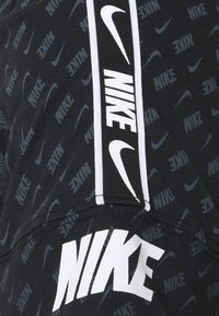 Svart idrottskläder med Nike-logomönster. Designen inkluderar en framträdande vit logga på framsidan och en randig detalj.