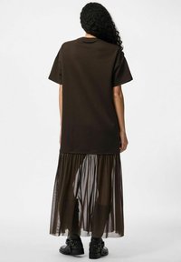 Brązowy, oversize t-shirt z krótkim rękawem, w połączeniu z półprzezroczystą brązową spódnicą maxi z siatki, charakteryzującą się warstwowym materiałem i zwiewnym fasonem.