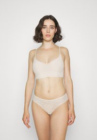 Bralette color beige chiaro con spalline sottili, design a V, abbinato a culotte coordinate in tessuto strutturato con un motivo ondulato. Tessuto morbido.