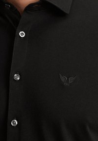 Czarny polo z bawełny, z guziczkowym zapięciem i subtelnym wytłoczonym logo na piersi. Gładka tekstura z dopasowanym krojem.