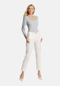 Grijze lange mouwen top met een gegolfde halslijn, gecombineerd met witte rechte broek. De outfit heeft een knoopsluiting en een getailleerde pasvorm.