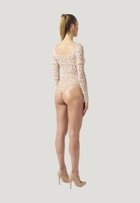 Body lungo nudo con maniche, caratterizzato da un motivo astratto beige chiaro, scollatura alta sul retro e design aderente, abbinato a tacchi alti nudi.