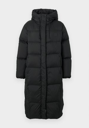 Hosszú fekete steppelt pufajka kapucnival, húzózsinórral, patent gombokkal és oldalsó patent zárakkal, a melegség és az időjárás elleni védelem érdekében tervezve.