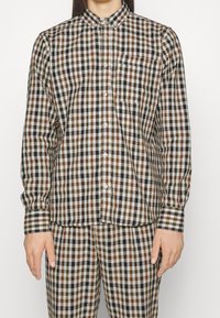 Brun och vit rutiga skjorta med krage, med långa ärmar och bröstficka, kombinerad med matchande rutig byxor.