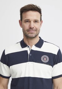 Pánska polo košeľa námorníckej a bielej pruhovanej farby, z bavlny, s krátkymi rukávmi, dvojité gombíky na zapínaní, vyšitý logo na hrudi.
