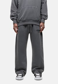 Gray cotton hoodie with a kangaroo pocket, loose-fit matching sweatpants, and black detailing on the waistband; paired with black and white sneakers.