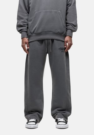 Gray cotton hoodie with a kangaroo pocket, loose-fit matching sweatpants, and black detailing on the waistband; paired with black and white sneakers.