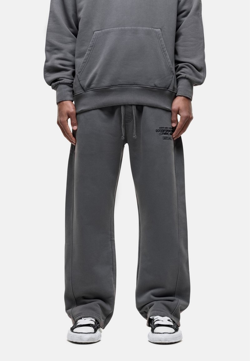 Gray cotton hoodie with a kangaroo pocket, loose-fit matching sweatpants, and black detailing on the waistband; paired with black and white sneakers.