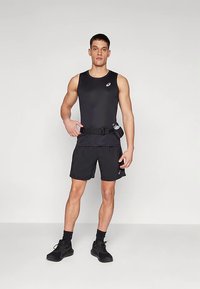 Črna atletska majica brez rokavov in kratke hlače z pasom za steklenico vode. Material je lahek; dizajn vključuje minimalistično blagovno znamko in elegantno prileganje.