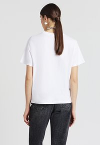 T-shirt bianca in cotone con maniche corte, taglio dritto e design minimalista. Il tessuto appare morbido con una consistenza liscia.