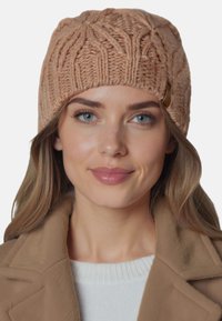 Strikket lys brun beanie med et kabelmønster og en lille dekorativ knap på siden. Blød tekstur, rund form og varmt design.