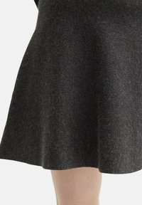 Juoda vilnonė sijonas su platėjančia forma, turi tekstūrinį paviršių ir subtilius, minkštus plaukus. Baigiasi vidurinėje šlaunies dalyje.