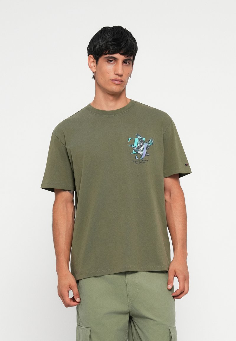 Oliven grøn bomulds T-shirt med korte ærmer. Forsiden har et grafisk print af fugle og logo. Rund halsudskæring og afslappet pasform.