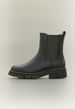 Stivale Chelsea in pelle nera con pannello laterale elastico, linguetta al tallone, suola spessa e robusta e tacco basso impilato su sfondo neutro.