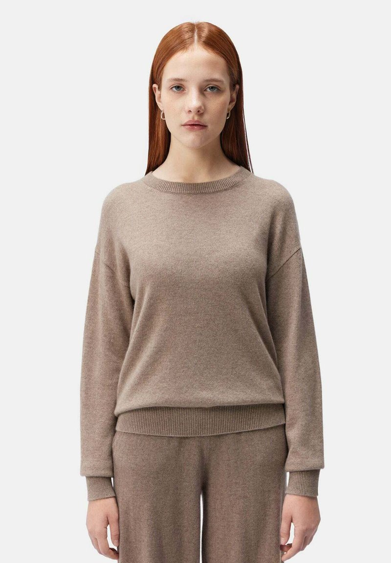 Pull en tricot marron clair avec un col rond, des épaules tombantes et des poignets côtelés, associé à un bas assorti pour un look harmonieux.
