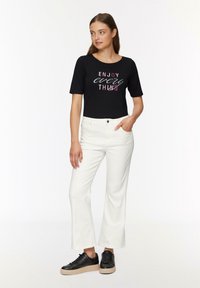 Black short-sleeve t-shirt with "ENJOY every THING" text in various colors, paired with white wide-leg jeans and black lace-up sneakers.
