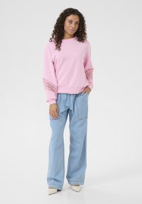 Rožinis džemperis su nėriniais ant rankovių, derinamas su šviesiai mėlynomis laisvomis džinsomis ir baltomis smailiomis bateliais.