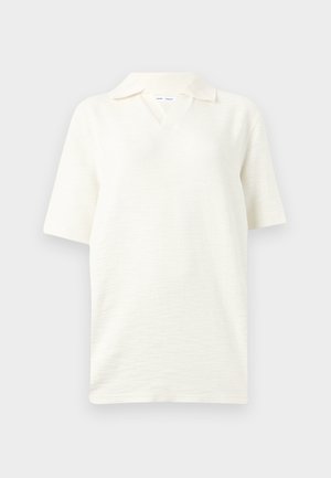 Polo blanc texturé à manches courtes avec un col doux et une ouverture en V, présenté sur un fond gris clair.