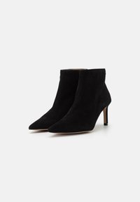 Botas de ante negras hasta el tobillo con punta afilada y tacón de aguja delgado. Textura suave, diseño minimalista y sin herrajes ni patrones visibles.