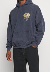 Sudadera azul marino hecha de algodón suave con un bolsillo canguro delantero. Presenta una impresión gráfica de un diseño de sol en el pecho.