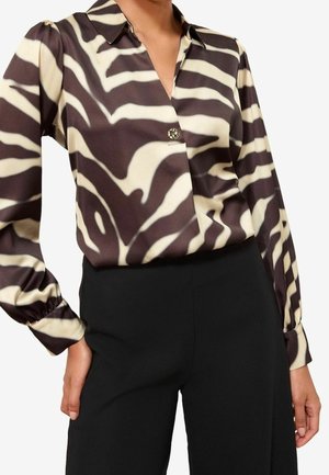 Femme portant un chemisier à manches longues imprimé zèbre noir et blanc, rentré dans un pantalon noir taille haute.