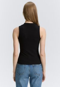 Schwarzes geripptes ärmelloses Oberteil mit hohem Kragen, figurbetontem Schnitt und glatter Textur, kombiniert mit hellblauen hoch taillierten Jeans.