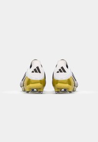 Des crampons de football avec une tige blanche, des rayures noires Adidas et un talon jaune brillant. Ils possèdent une surface texturée et des pointes transparentes sur la semelle.