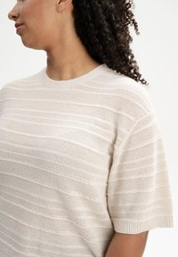 Lichtbeige gebreide top met een gewatteerd, gestreept patroon, ronde halslijn en korte mouwen. Zachte, ademende stof.