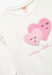 Hvid sweatshirt med to broderede hjerter i pink og lys pink, med smilende ansigt og teksten "mamas lille stjerne" nedenfor.