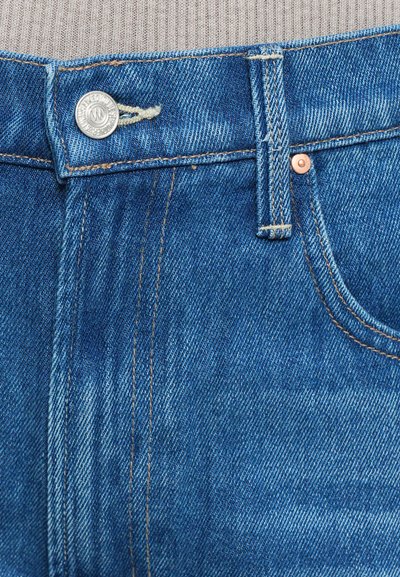 Close-up of blue denim jeans waistband with metal button, belt loop, front pocket, and visible stitching details.