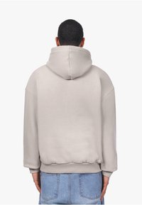 Hellgrau oversized Kapuzenpullover mit Kängurutasche, fallenden Schultern, geripptem Saum und Bündchen. Weicher Stoff ohne sichtbare Muster.