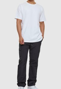 Bílé bavlněné tričko s krátkým rukávem v kombinaci s černými pracovními kalhotami s bočními kapsami a pohodlným střihem, doplněné bílými teniskami.