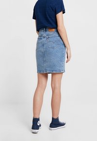 Vaaleansininen farkuhame, jossa on korkea vyötärö, polvipituinen malli, takana paikka ja kaksi takataskua. Yhdistettynä tummansiniseen t-paitaan ja lenkkareihin.