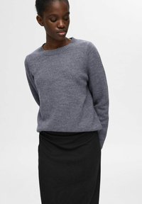 Grå uldtrøje med rund halsudskæring og lange ærmer, parret med en sort blyantskirt. Blød tekstur og tætsiddende design.