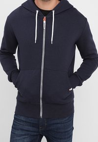 Námořnická mikina na zip s předním zipem, kapucí na stažení šňůrkou a dvěma předními kapsami. Vyrobeno z texturované látky. Bílé detaily na zipu.