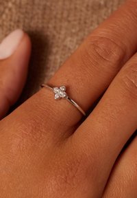 Zilveren ring met een delicate bloemdesign, voorzien van vier heldere stenen in het midden, gezet op een dunne, gepolijste band.