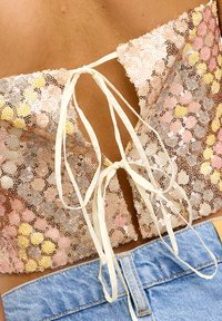 Pailletten crop top met een sluiting op de rug. Heeft veelkleurige ronde pailletten in goud, roze en zilver op een doorzichtige stof. In combinatie met denim shorts.