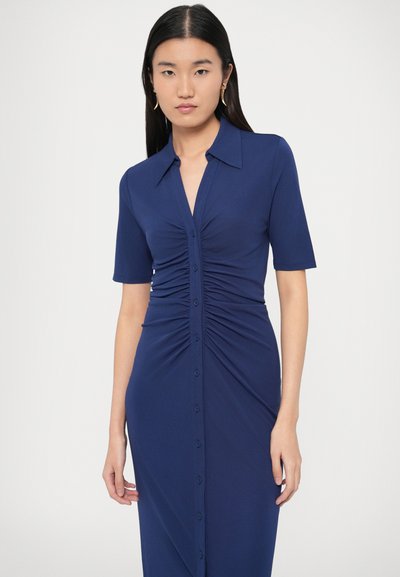 Dopasowana granatowa sukienka z krótkimi rękawami, z przodu zapinana na guziki oraz z marszczeniem w talii, które podkreśla sylwetkę. Gładka faktura.