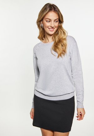 Grå sweater med lange ærmer, der har dekorative knapper på skulderen. Sammen med en sort nederdel, der viser et tætsiddende design.