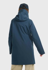 Manteau long en bleu imperméable avec col haut et capuche. Présente des manches amples et une coupe droite. Le matériau semble lisse et durable.